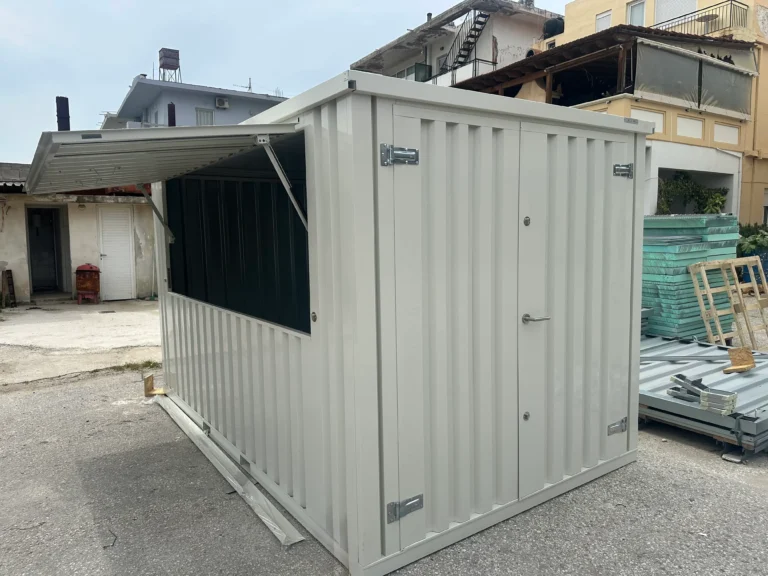 A grey shipping container modified with a large lift-up serving window, placed in an outdoor industrial area.