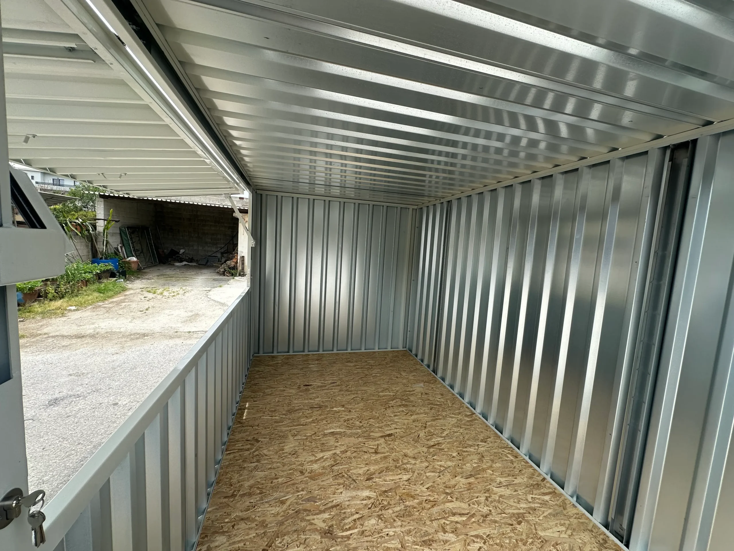 A grey shipping container modified with a large lift-up serving window, placed in an outdoor industrial area.